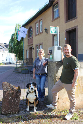 Steffi Horbach und Ortsvorsteher Thomas Müller am neuen Defibrillator, der zentral gelegen an der Sötenicher Obermühle allen zur Verfügung steht, die Erste Hilfe leisten.